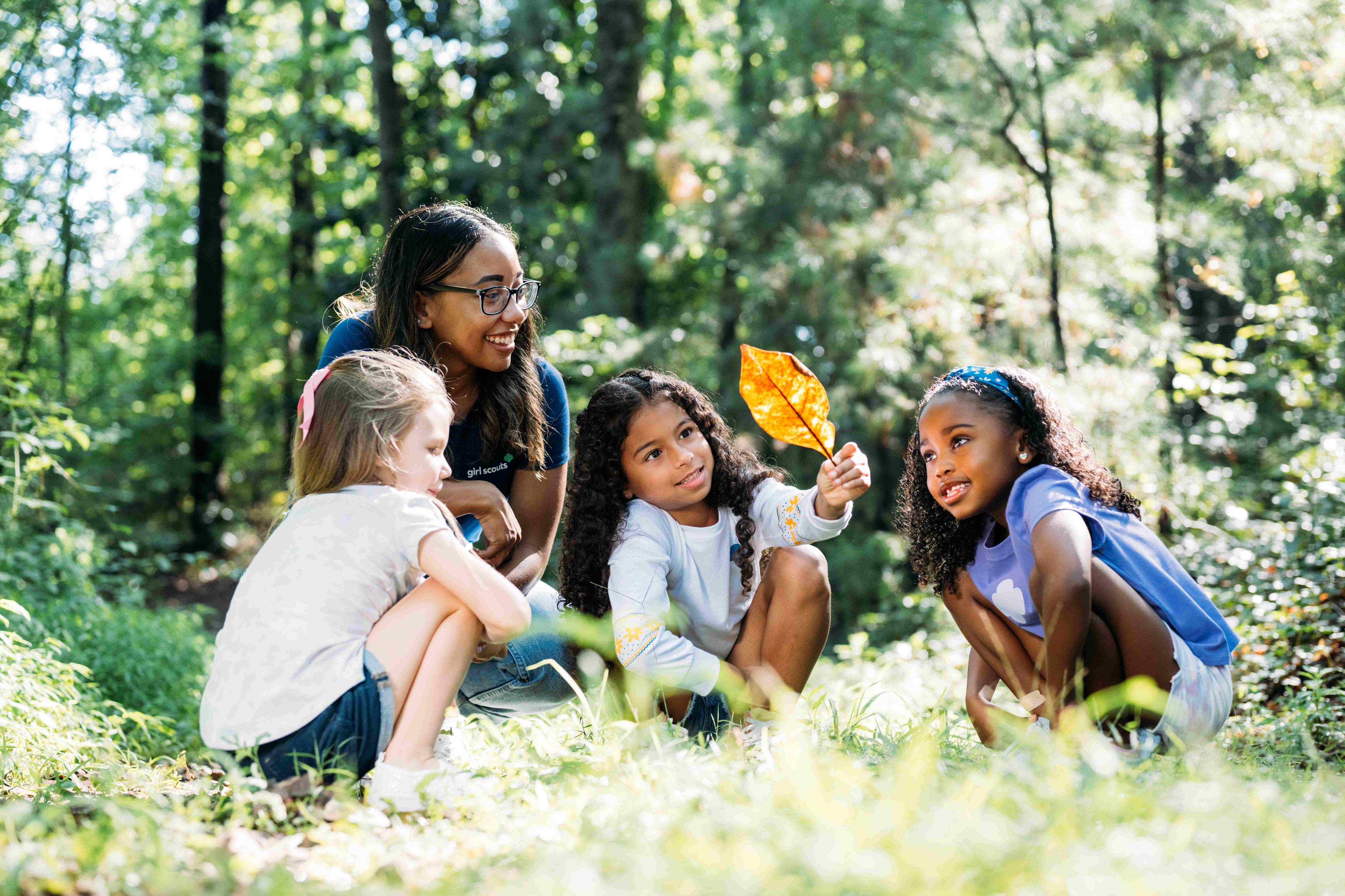A group of Girl Scouts spending time outdoors and learning about nature with their troop leader.